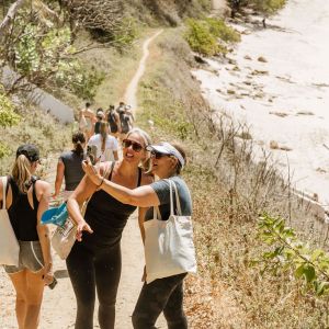 Two women taking a selfie on a coastal trail with others walking behind them.