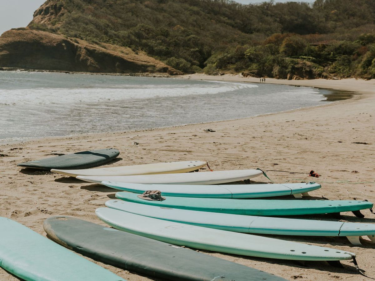 Surfboards on a sandy beach with a rocky hill in the background.
