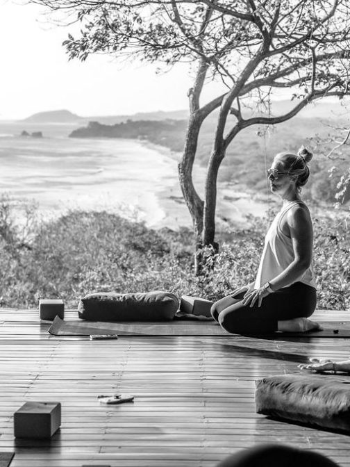 People practicing yoga on a wooden deck overlooking a scenic coastline.