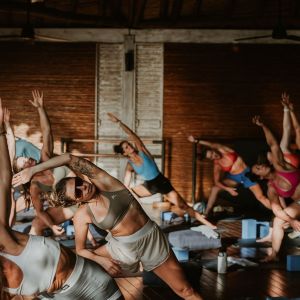Group of people doing yoga in a wooden studio, performing side stretches.