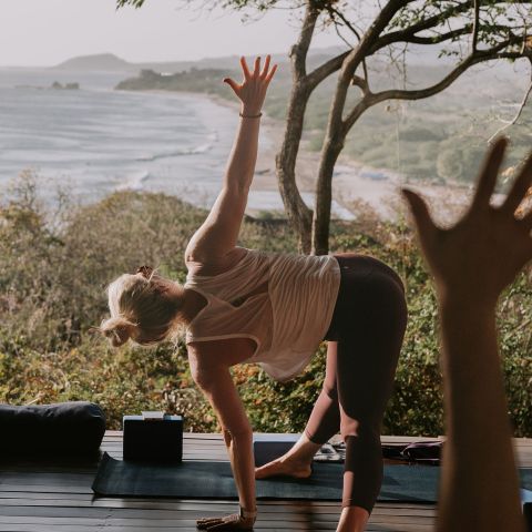 Person practicing yoga outdoors with ocean view background.