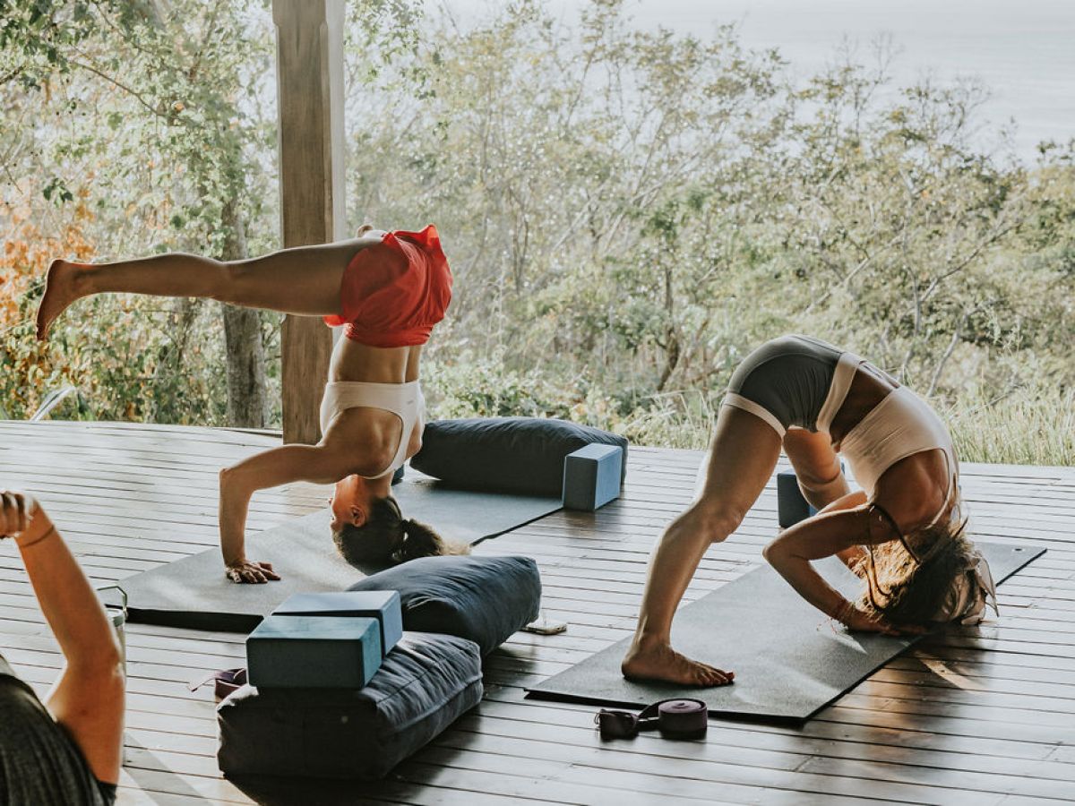 Two people practicing yoga on a wooden deck with trees in the background.