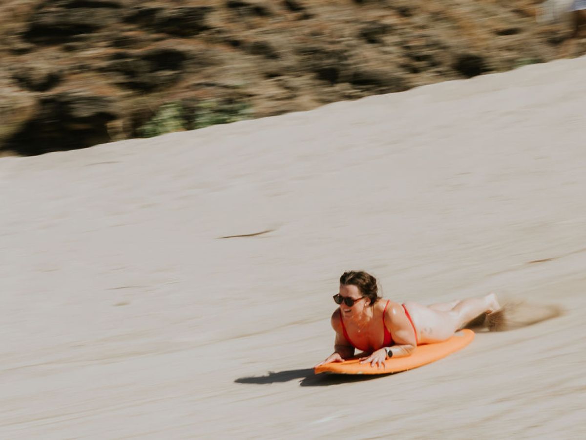 Person sliding down a sandy hill on an orange bodyboard.