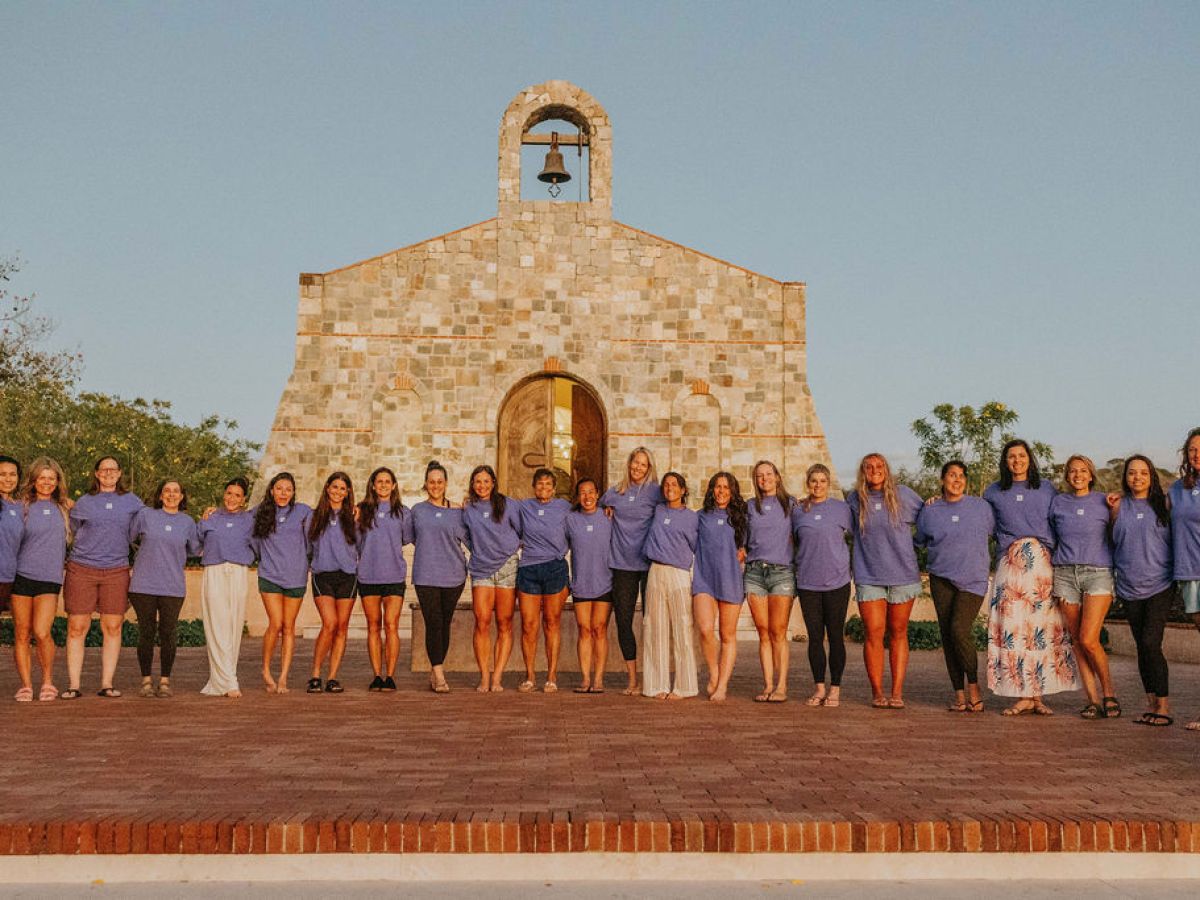Group of people in blue shirts standing in front of a stone chapel.