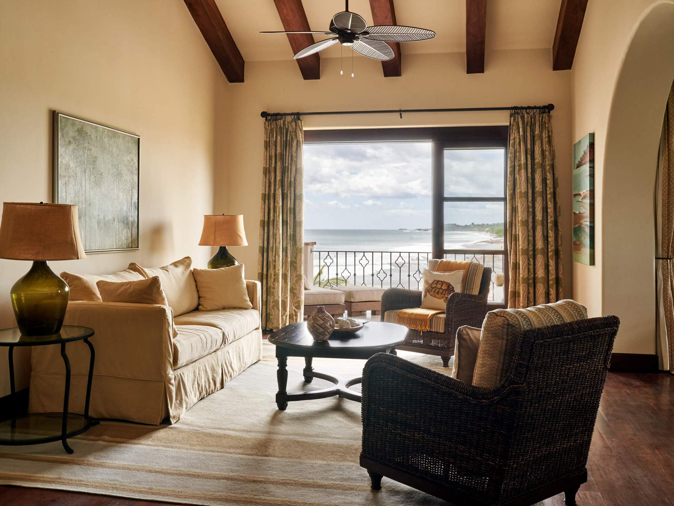 Cozy living room with sea view, sofa, chairs, and ceiling fan.