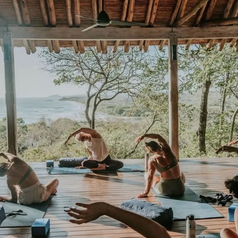 People doing yoga on a wooden deck with a scenic ocean view.