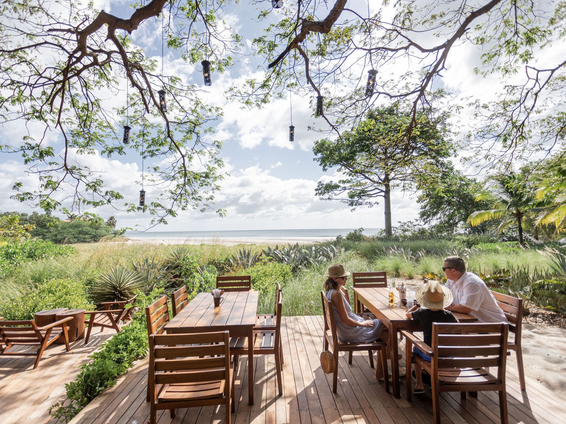 Two people dining outdoors at a wooden table with a beach view.