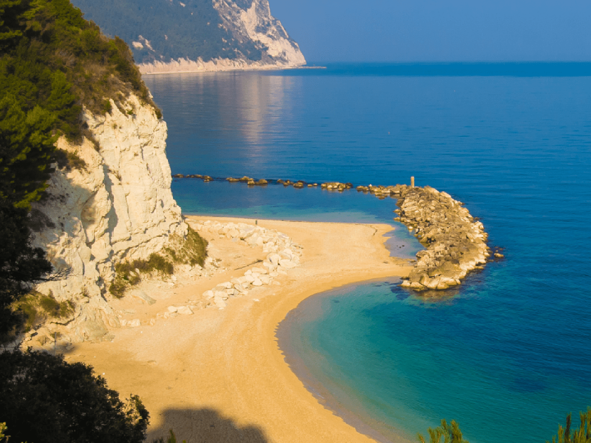 Scenic beach with cliffs, turquoise water, and land formations in sunlight.