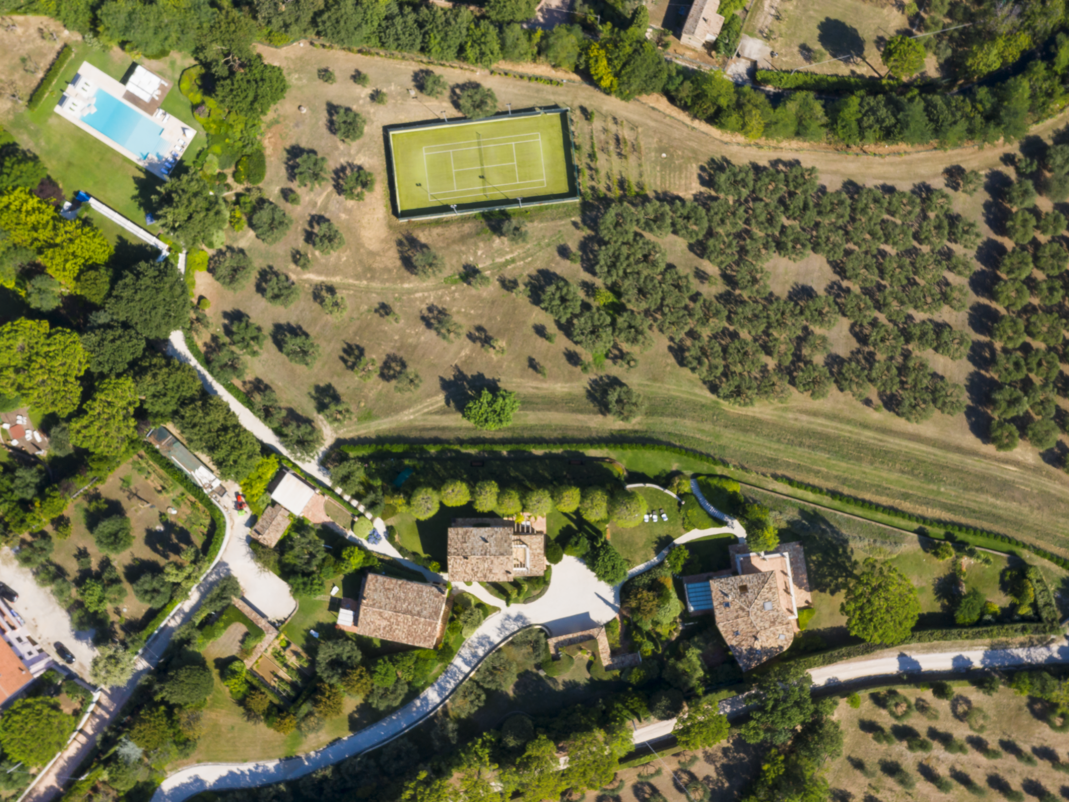 Aerial view of a rural landscape with buildings, tennis court, pool, and trees.