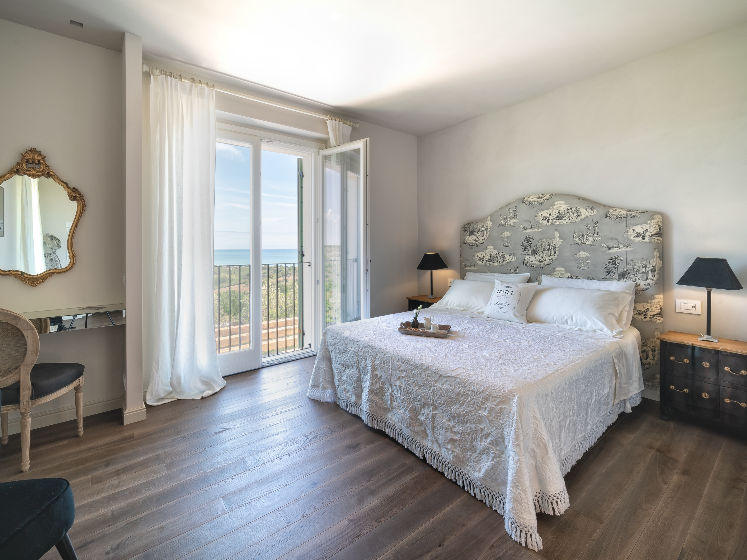 Bright bedroom with large bed, ornate mirror, and balcony view.