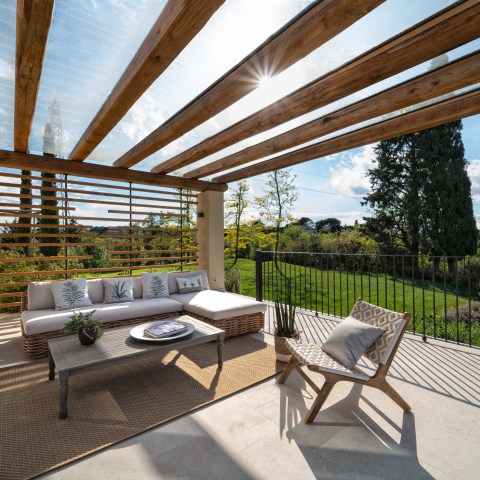 Outdoor patio with wooden pergola, sofa, chairs, table, and view of garden.