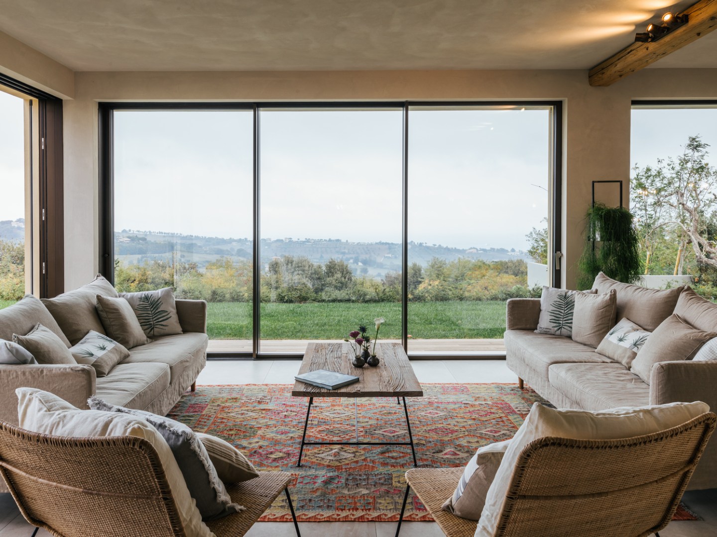 Cozy living room with large windows, sofas, armchairs, and a view of nature.
