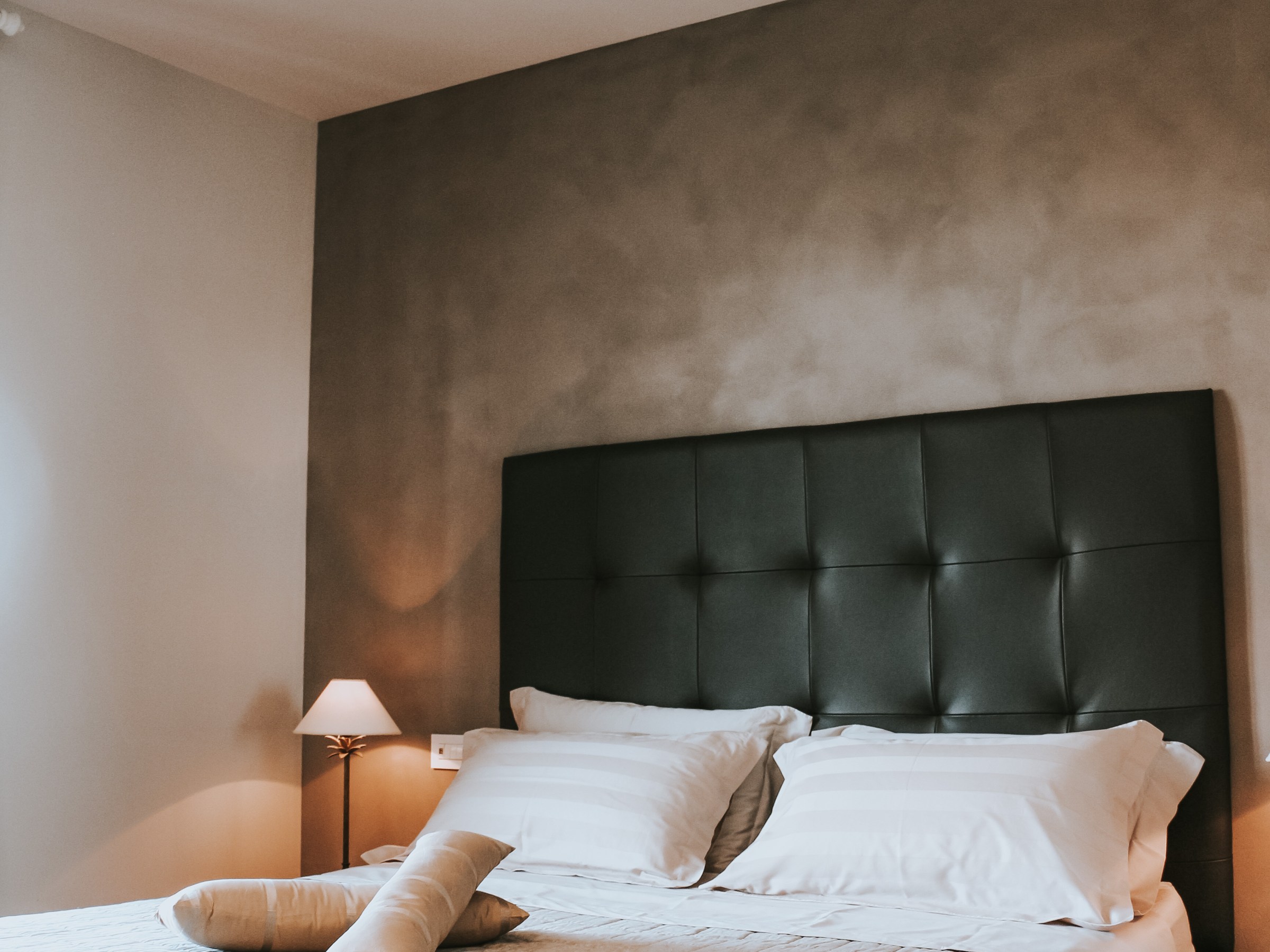 Modern bedroom with a gray upholstered headboard, white bedding, and a small bedside lamp.