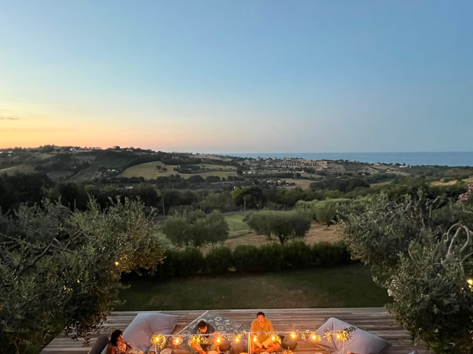 People dining on a deck with a scenic landscape view at sunset.