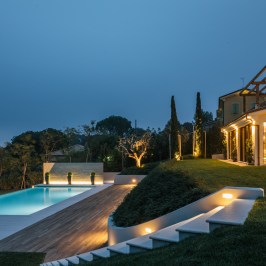 Modern house with pool and garden at dusk, softly lit.