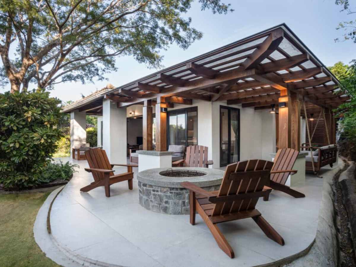 Outdoor patio with wooden chairs around a stone fire pit under a pergola.