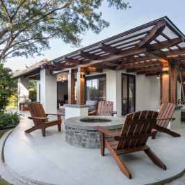 Outdoor patio with wooden chairs around a stone fire pit under a pergola.