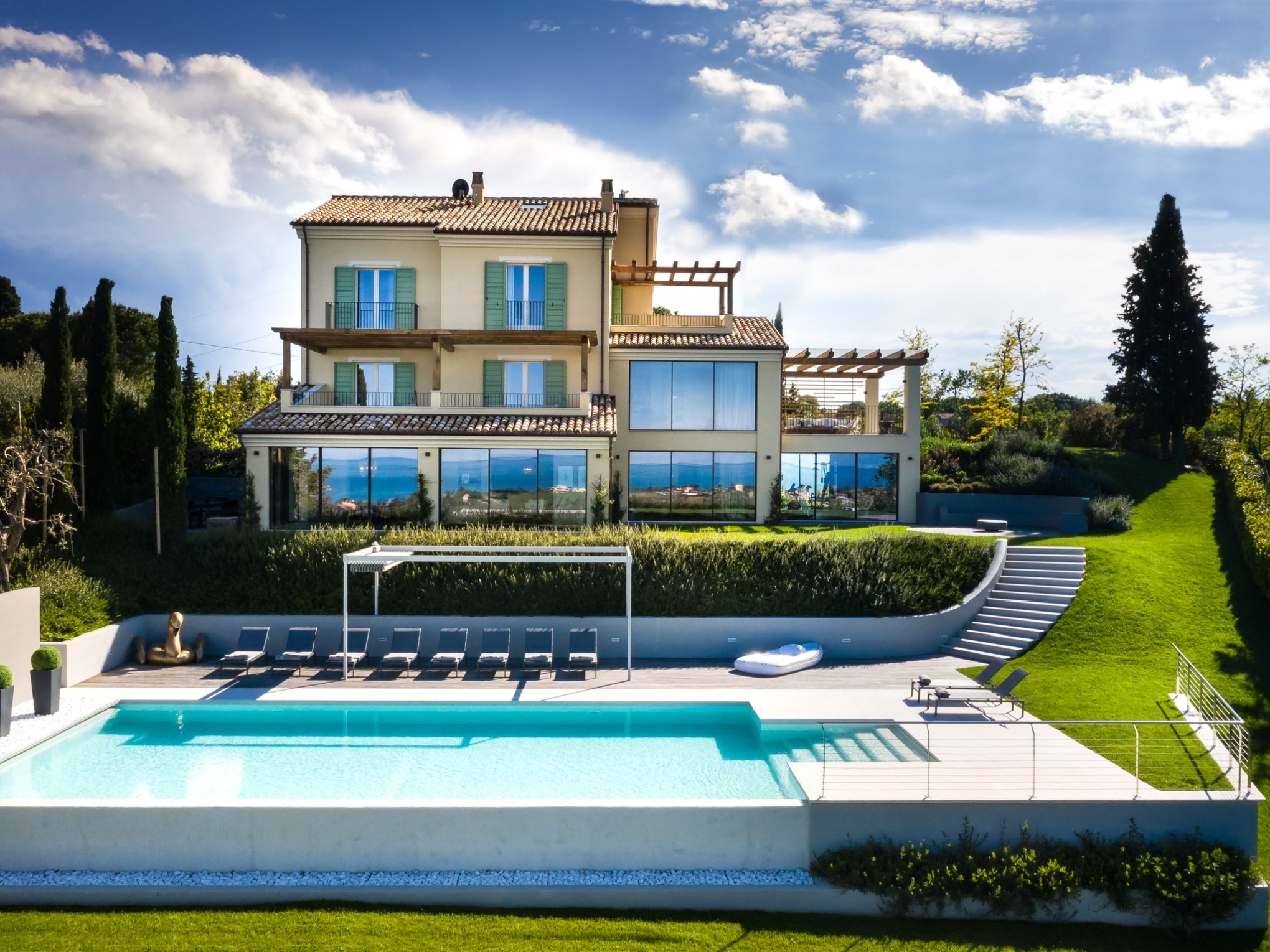 Luxurious house with large windows, pool, and landscaped yard under a blue sky.