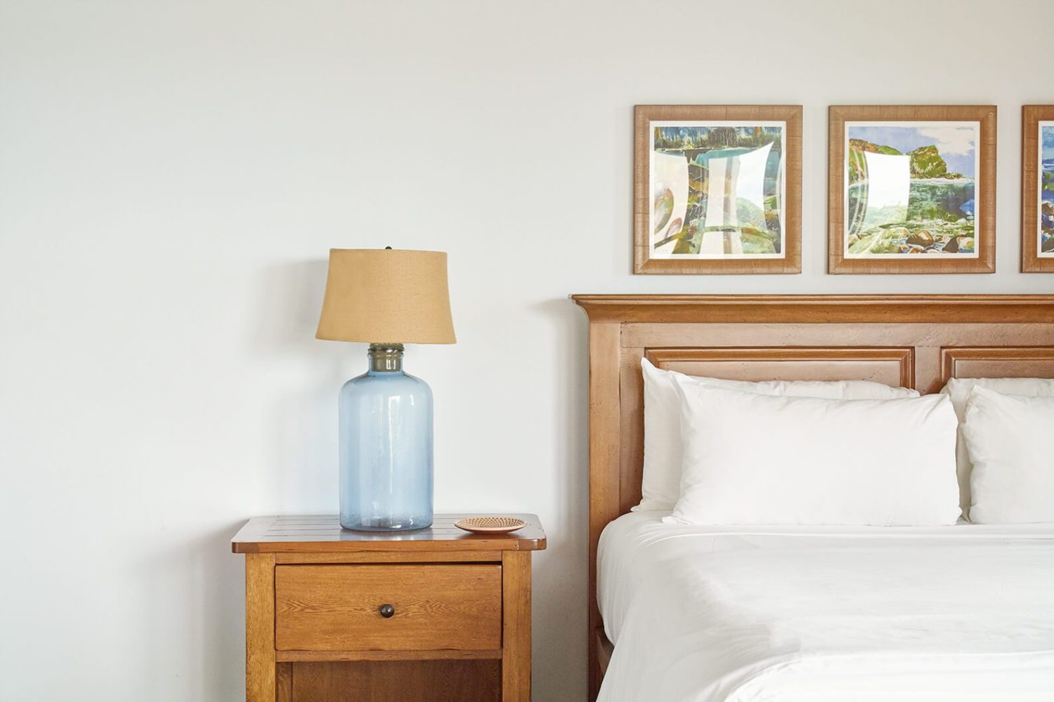 Bedroom with wooden bed, side table, blue lamp, and framed pictures on wall.
