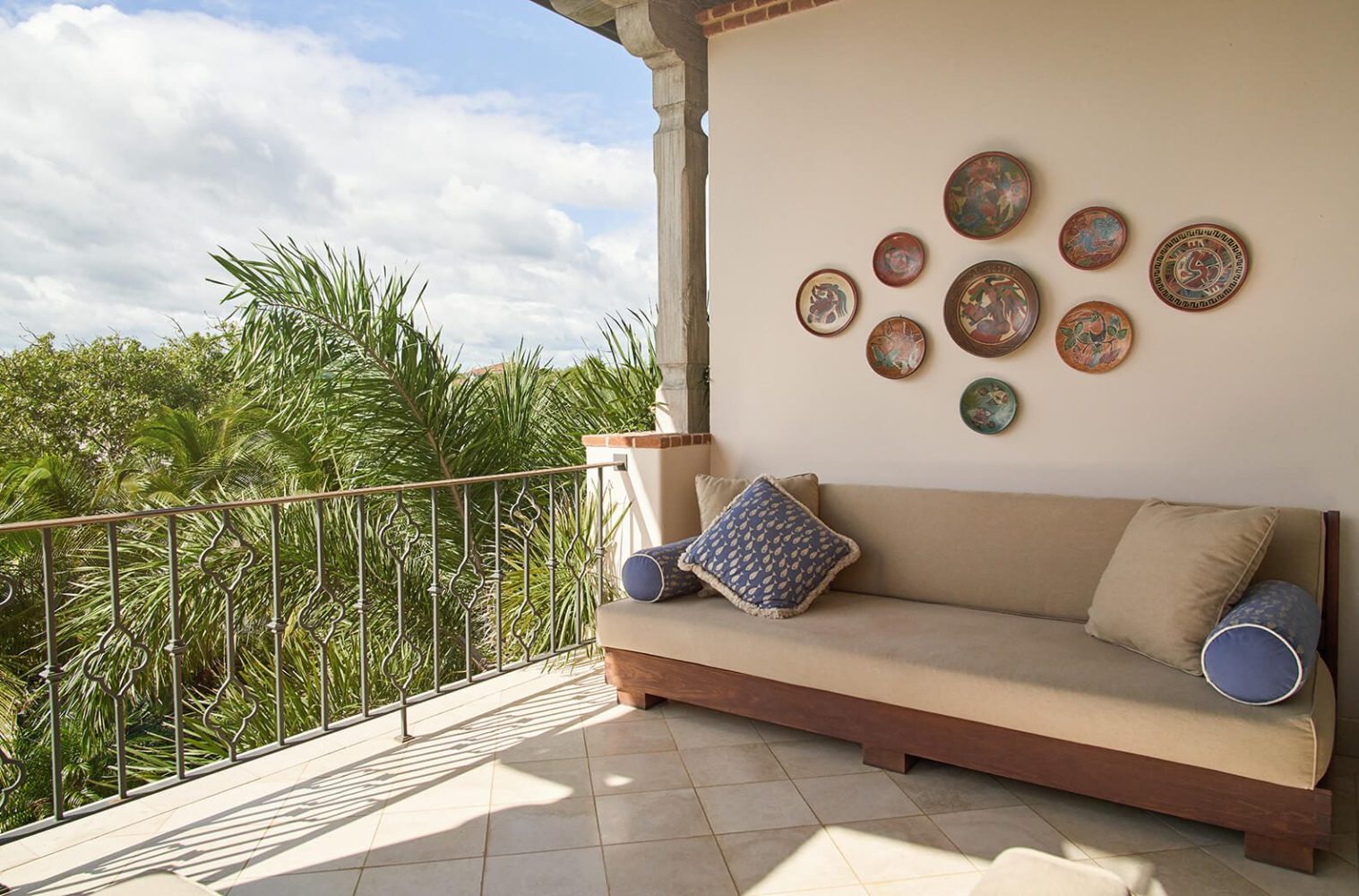 Outdoor patio with a sofa, decorative plates on wall, and view of palm trees.