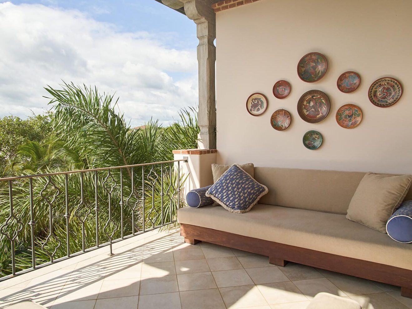 Outdoor patio with a sofa, decorative plates on wall, and view of palm trees.