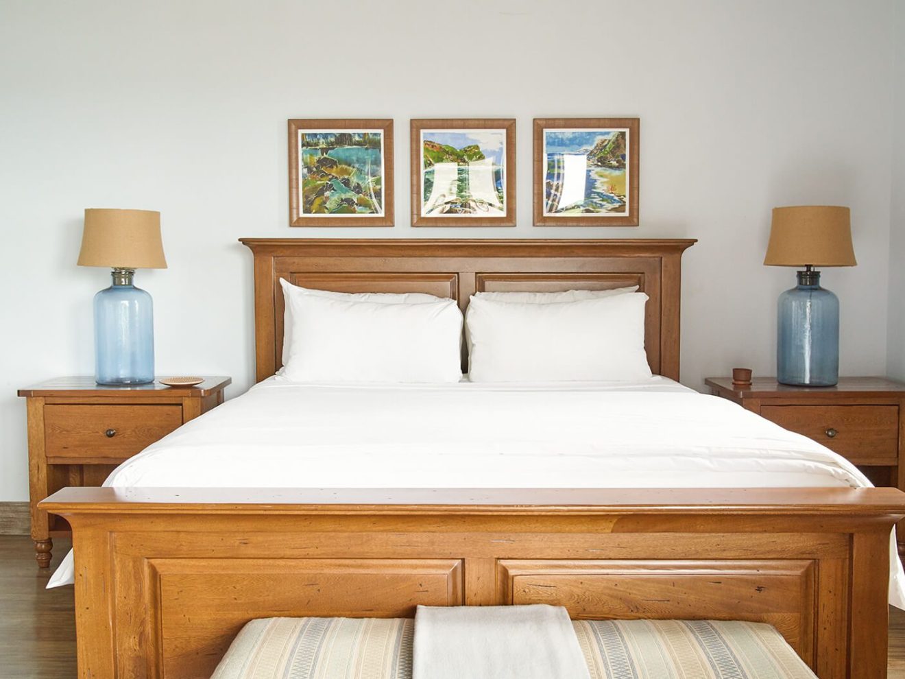 Wooden bed with white linens, flanked by blue lamps on nightstands.