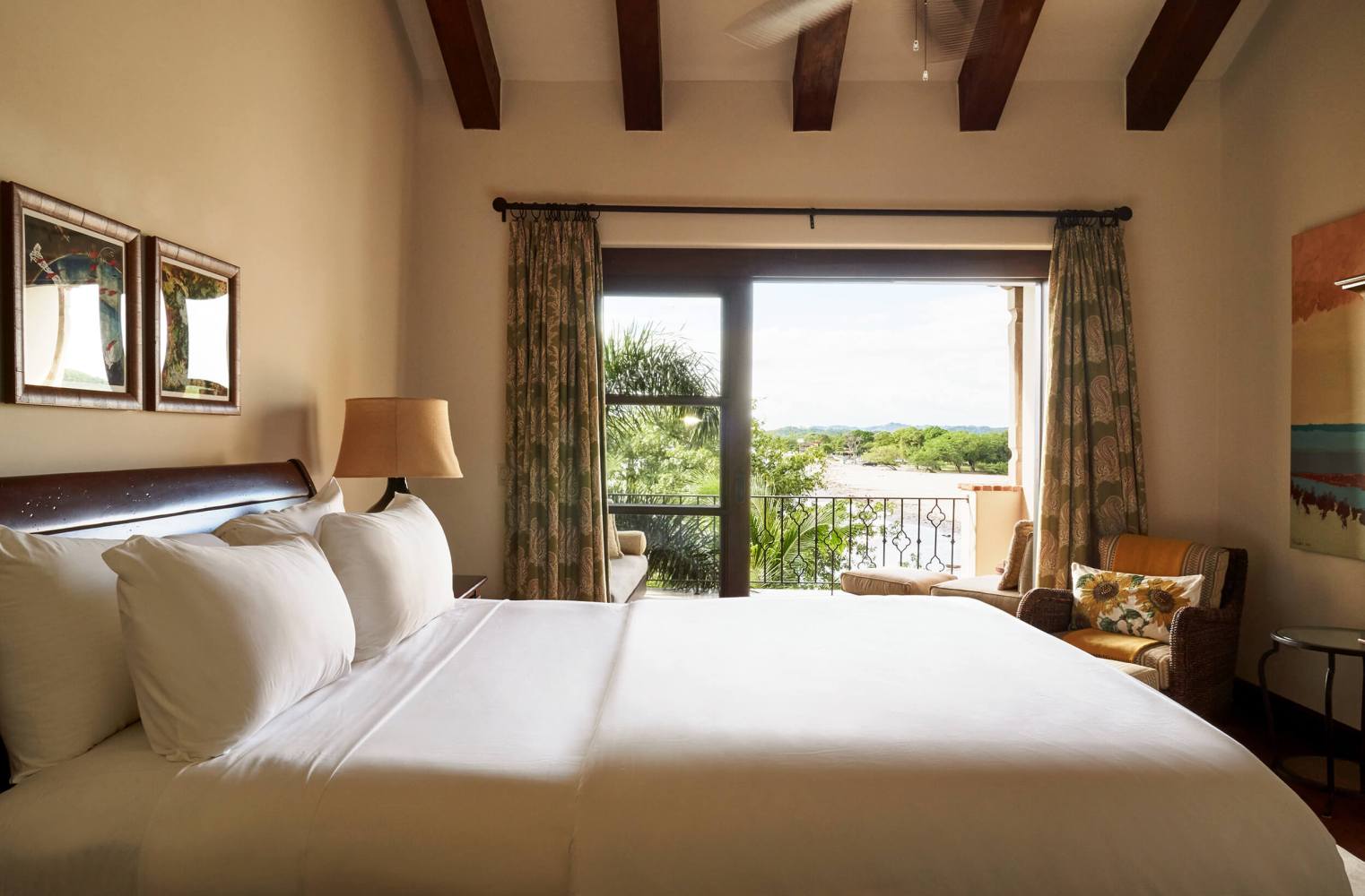 Cozy bedroom with large bed, wooden beams, and window view of trees.