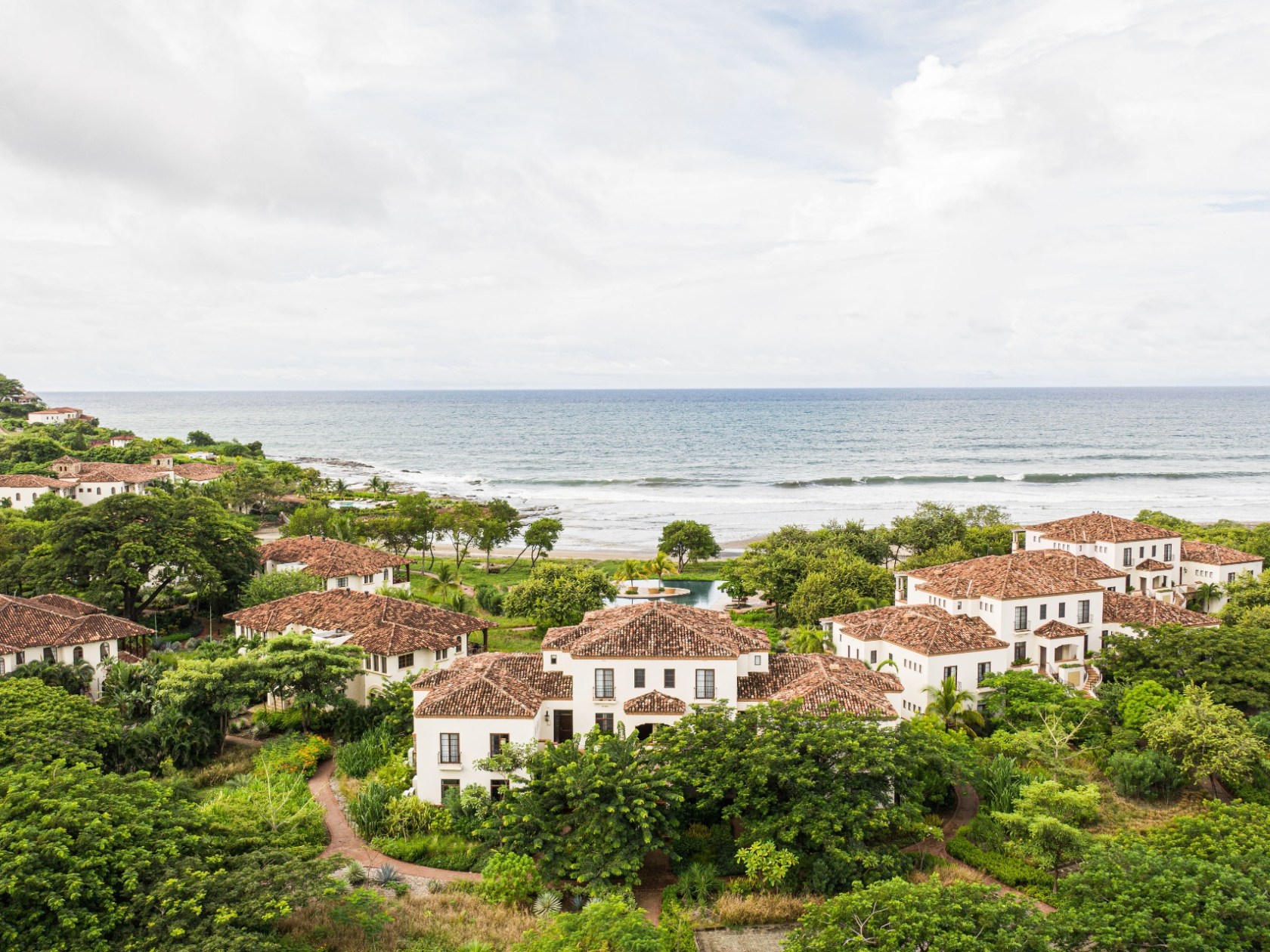 Coastal villas with red roofs surrounded by greenery near ocean.