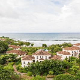 Coastal villas with red roofs surrounded by greenery near ocean.
