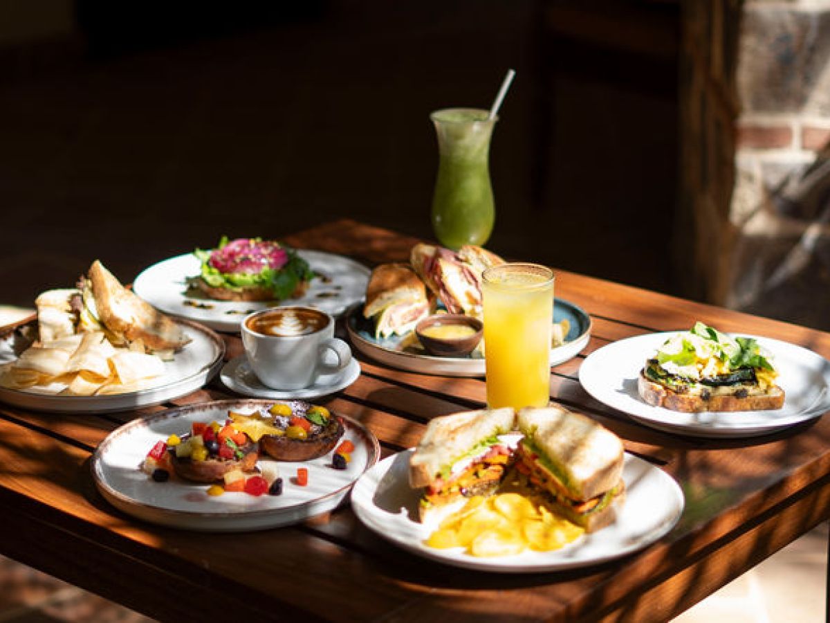 Assorted breakfast dishes on a wooden table with juices and coffee.