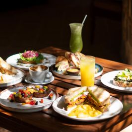 Assorted breakfast dishes on a wooden table with juices and coffee.