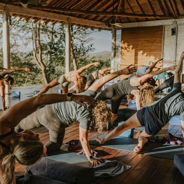 Group doing yoga stretches on mats in a wooden open-air pavilion.