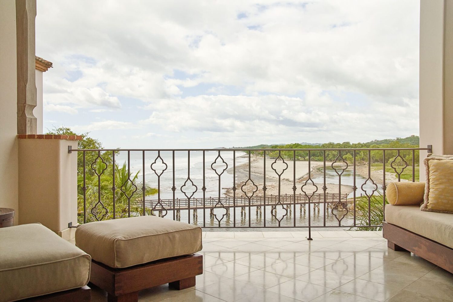 Balcony with ocean view and cushioned seating under cloudy sky.