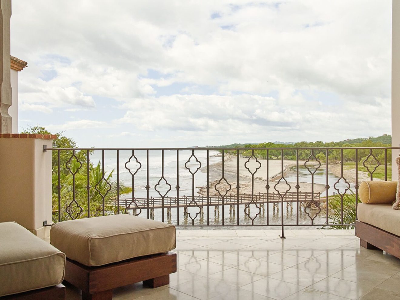 Balcony with ocean view and cushioned seating under cloudy sky.