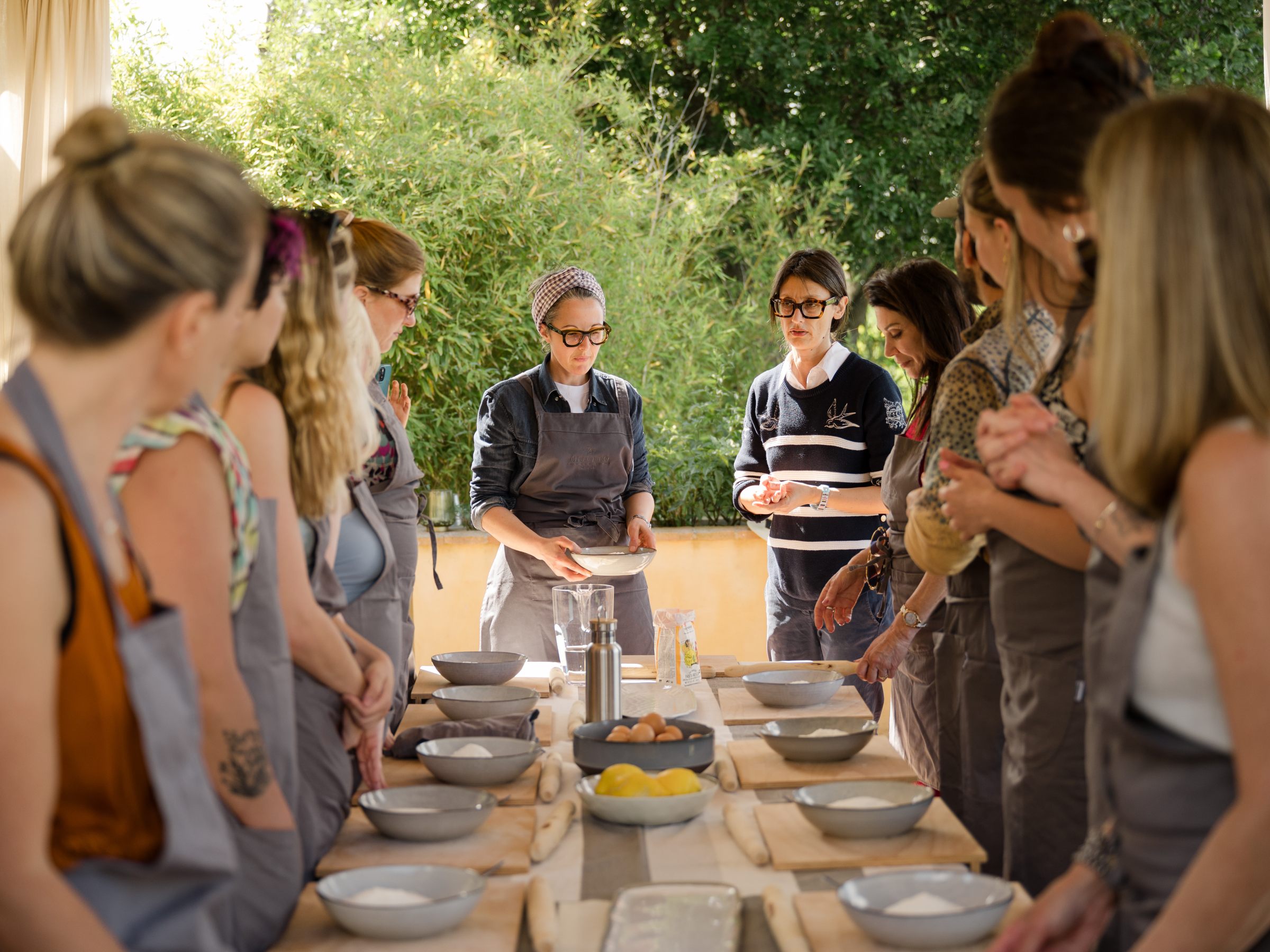 Group cooking class outdoor, instructor at the table's end with participants on both sides.