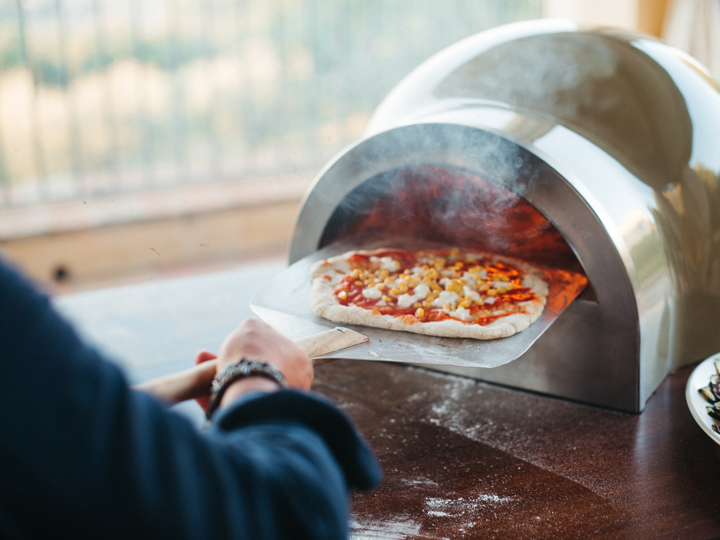 Person using a peel to remove a pizza from a metal pizza oven.