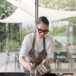 Smiling person in apron cooking, with outdoor background and table setup.