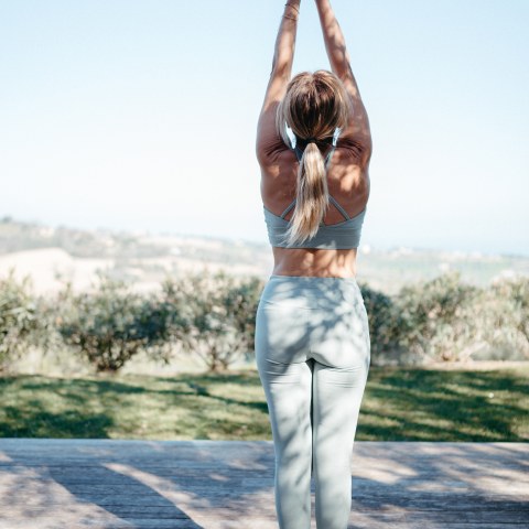 Woman practicing yoga outdoors, arms raised, standing on a mat.