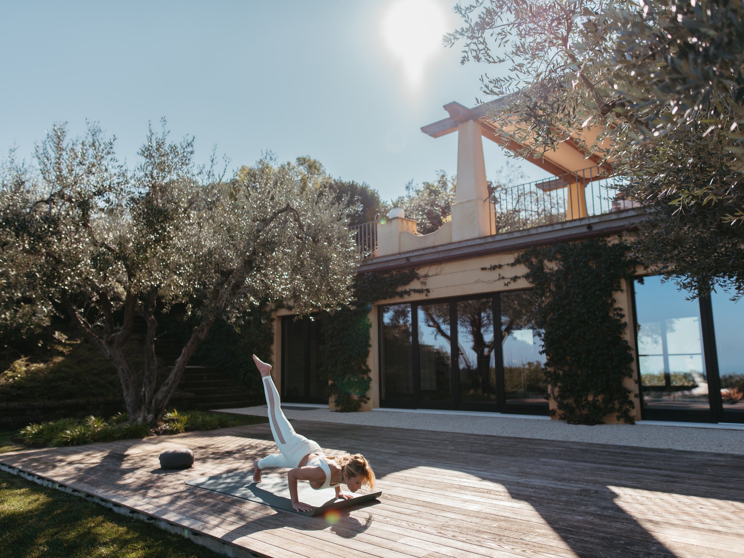 Person doing yoga on a wooden deck outside a modern house under the sun.