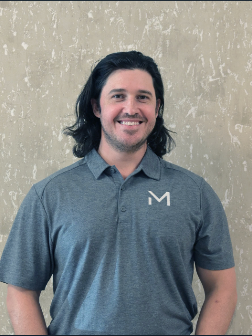 Smiling man with long hair in gray polo shirt against textured wall.