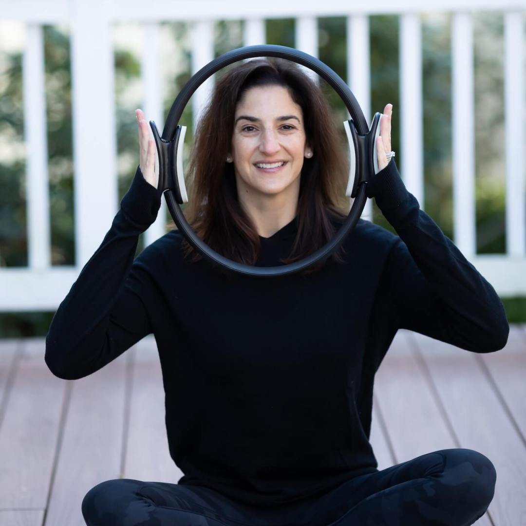 Jessica Newshel sitting cross-legged, holding a circular exercise ring over their face.