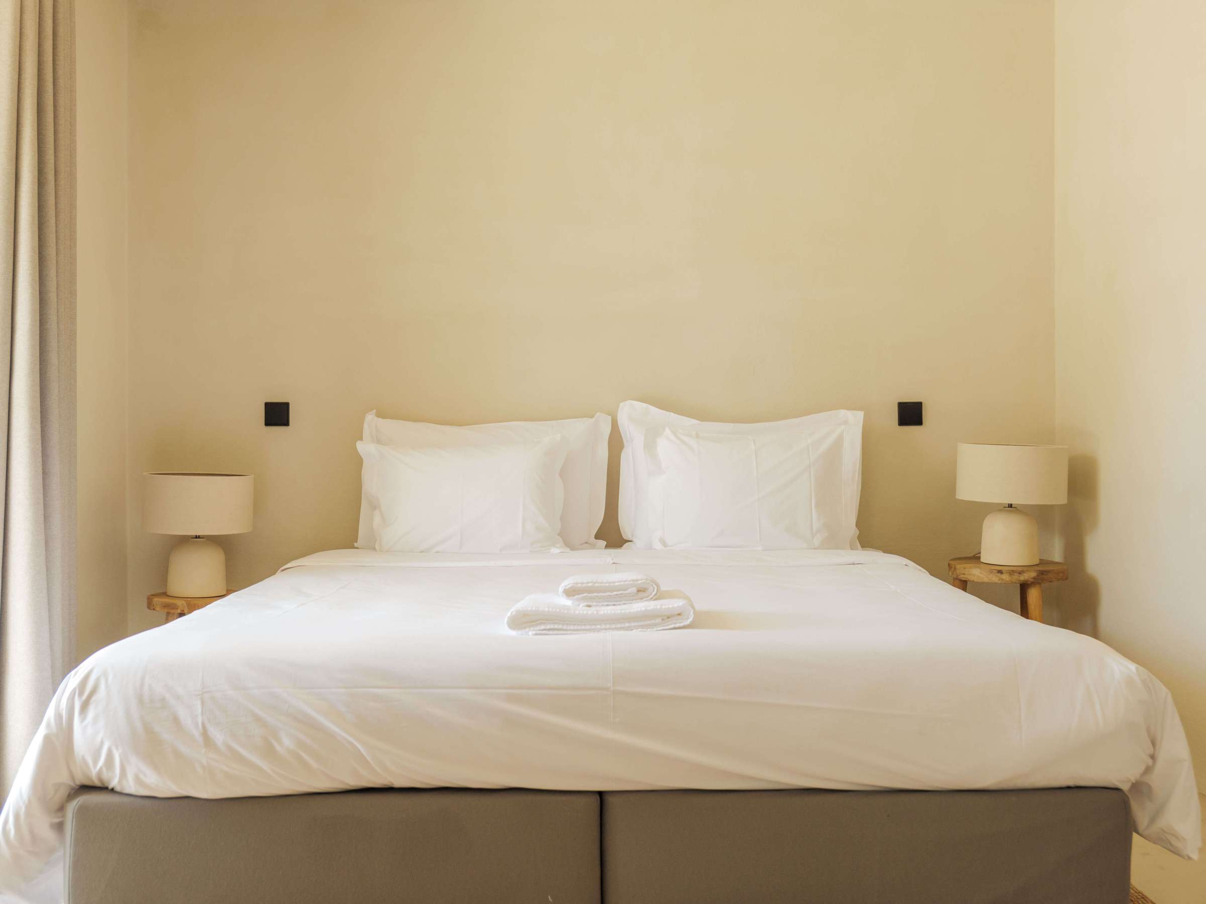 Minimalist bedroom with a neatly made double bed, white linens, and two bedside lamps.