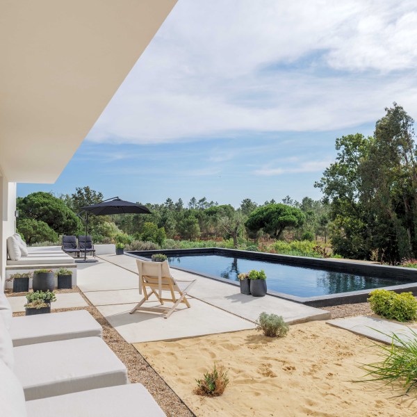 Modern patio with seating, pool, and garden view under clear sky.