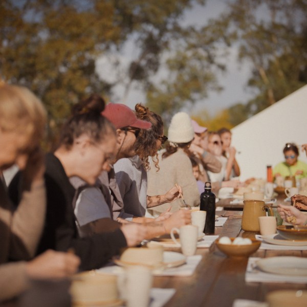 People dining outdoors at a long table with plates and a wine bottle.