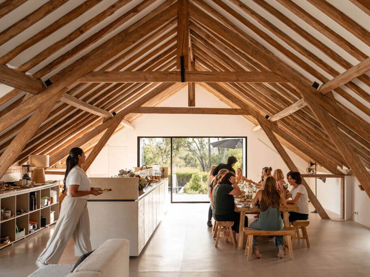 Cozy attic dining area with wooden beams, people eating at a long table, person serving food.