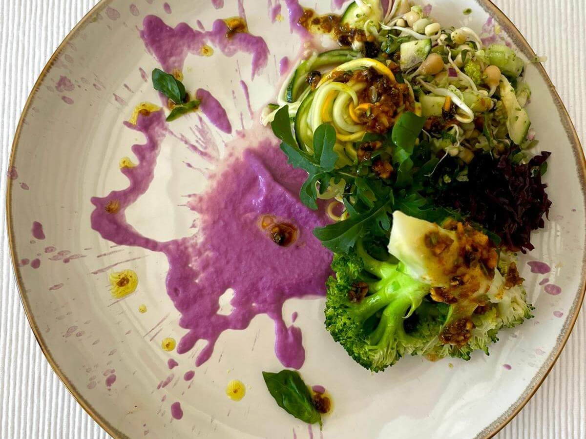 Artistic vegetable dish with purple sauce on a round plate.