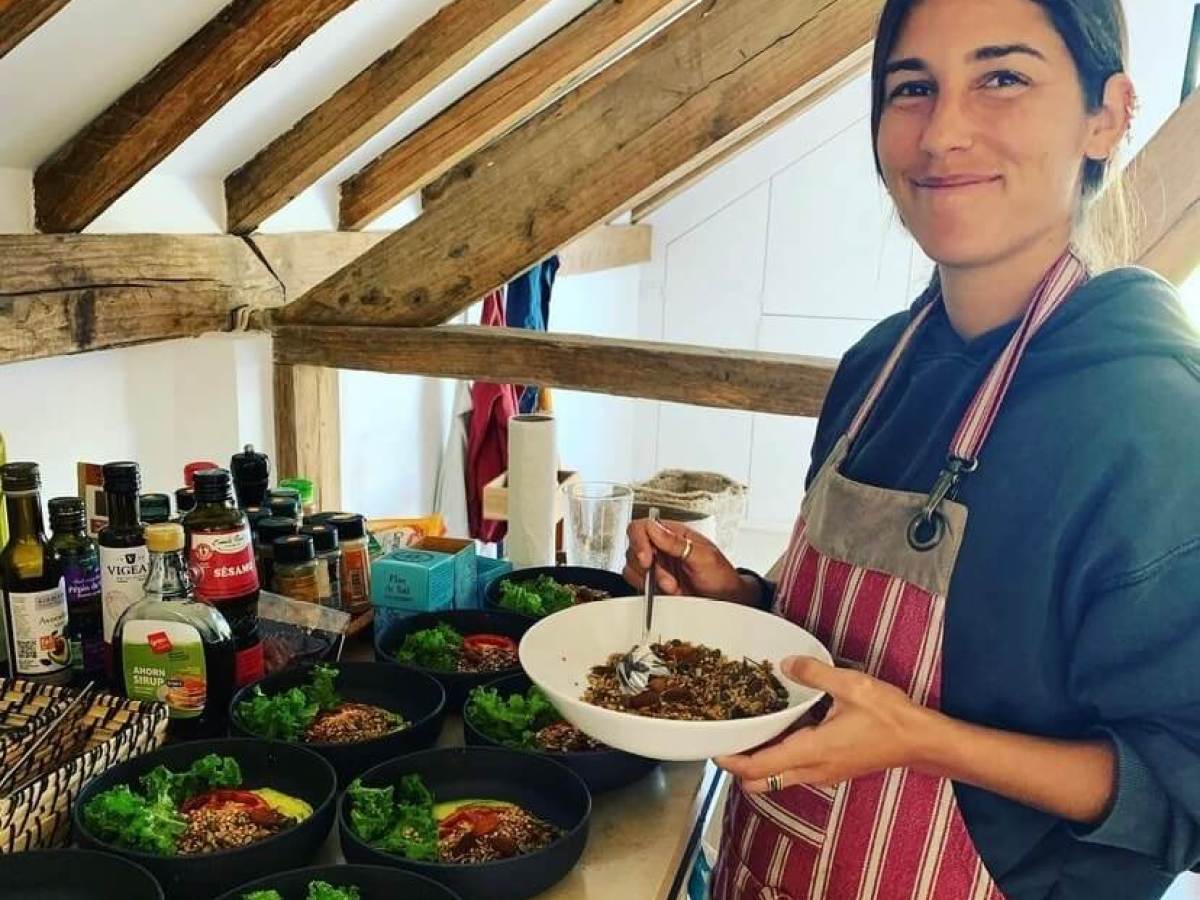 Person wearing an apron, holding a bowl, standing by a kitchen counter with several dishes.