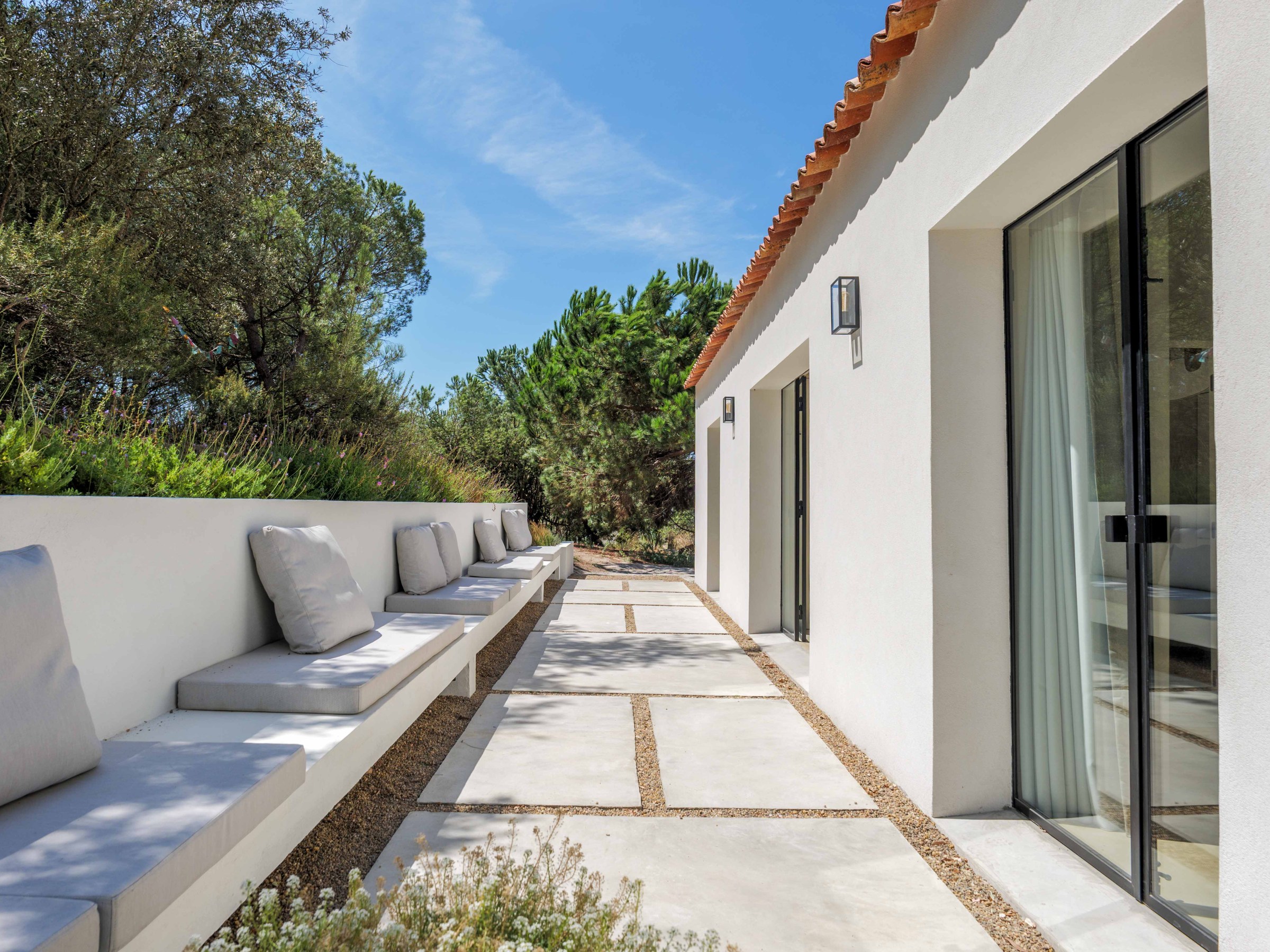 Modern patio with white benches and cushions alongside a house.