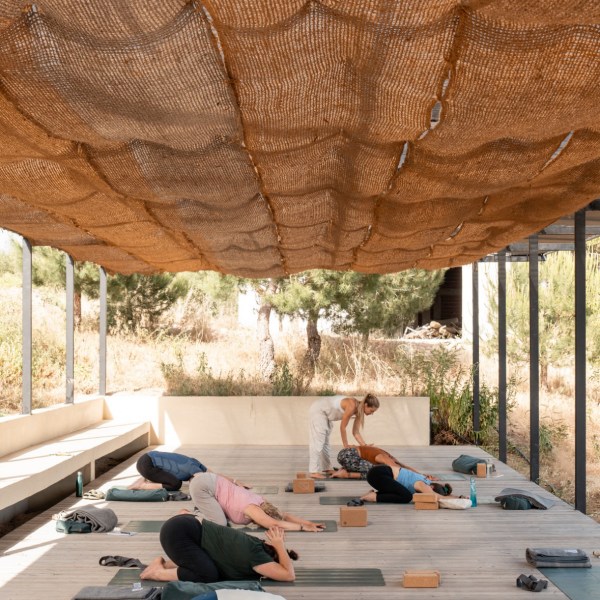People practicing yoga outdoors under a woven canopy.