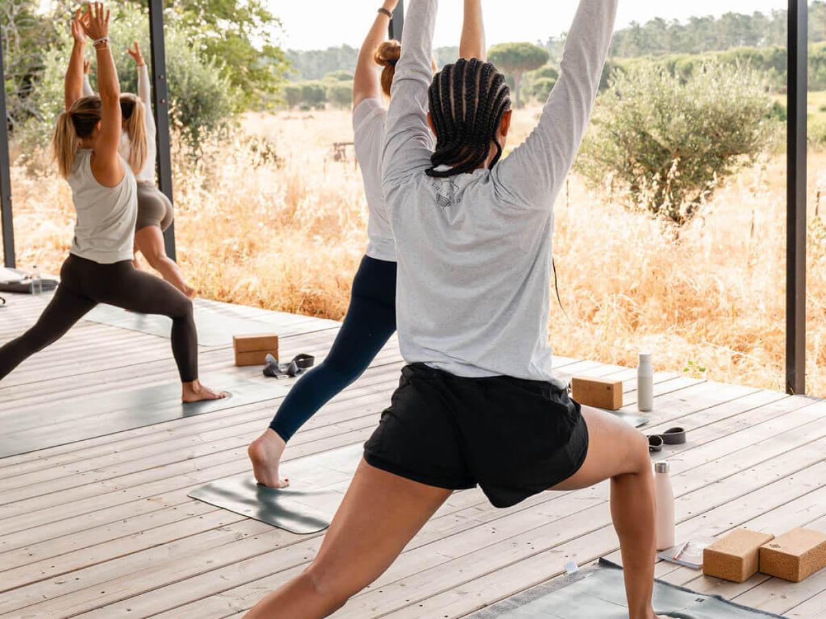 People practicing yoga outdoors in warrior pose on wooden deck.